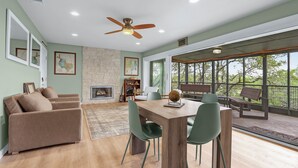 A spacious living room with a fireplace, a dining area with a wooden table and chairs, and large windows offering a view of the outdoors. - Hot Tub, EV Charger, Plus Stunning Hill Country Stargazing & Wildlife (Spring Branch)