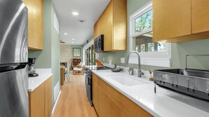 A modern kitchen with stainless steel appliances, wooden cabinets, and a large window. - Hot Tub, EV Charger, Plus Stunning Hill Country Stargazing & Wildlife (Spring Branch)