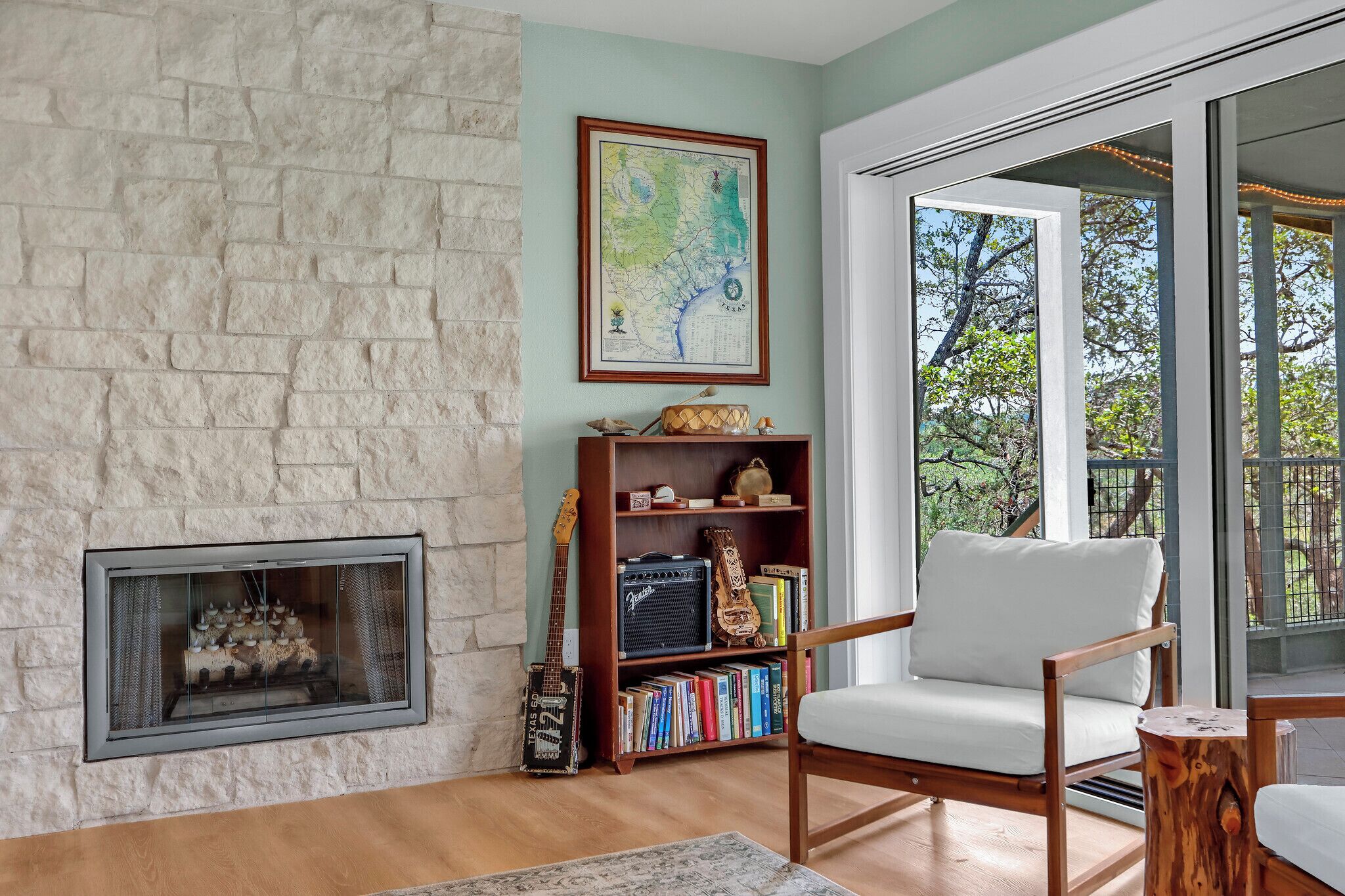 A living room with a stone fireplace, a bookshelf, a guitar, and a chair.