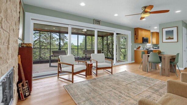 A spacious living area with a large window, a ceiling fan, and a dining table with chairs. - Hot Tub, EV Charger, Plus Stunning Hill Country Stargazing & Wildlife (Spring Branch)