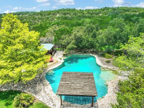 A clear blue pool surrounded by lush greenery, with a wooden structure in the foreground. - Luxury Ranch w/ Pool + Outdoor Living in Wimberley (Wimberley)