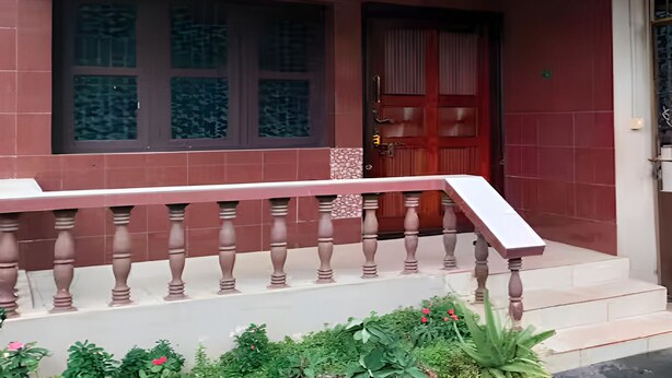Un bâtiment à l’extérieur rouge, avec une porte en bois et une fenêtre ornée de motifs dans le verre.