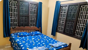 Une chambre à coucher avec un lit, une tête de lit en bois et deux fenêtres dotées de grilles en métal.