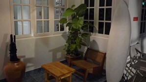 Una habitación con piso de baldosas, una mesa de madera, un banco, una planta en maceta y una tabla de surf apoyada contra la pared.