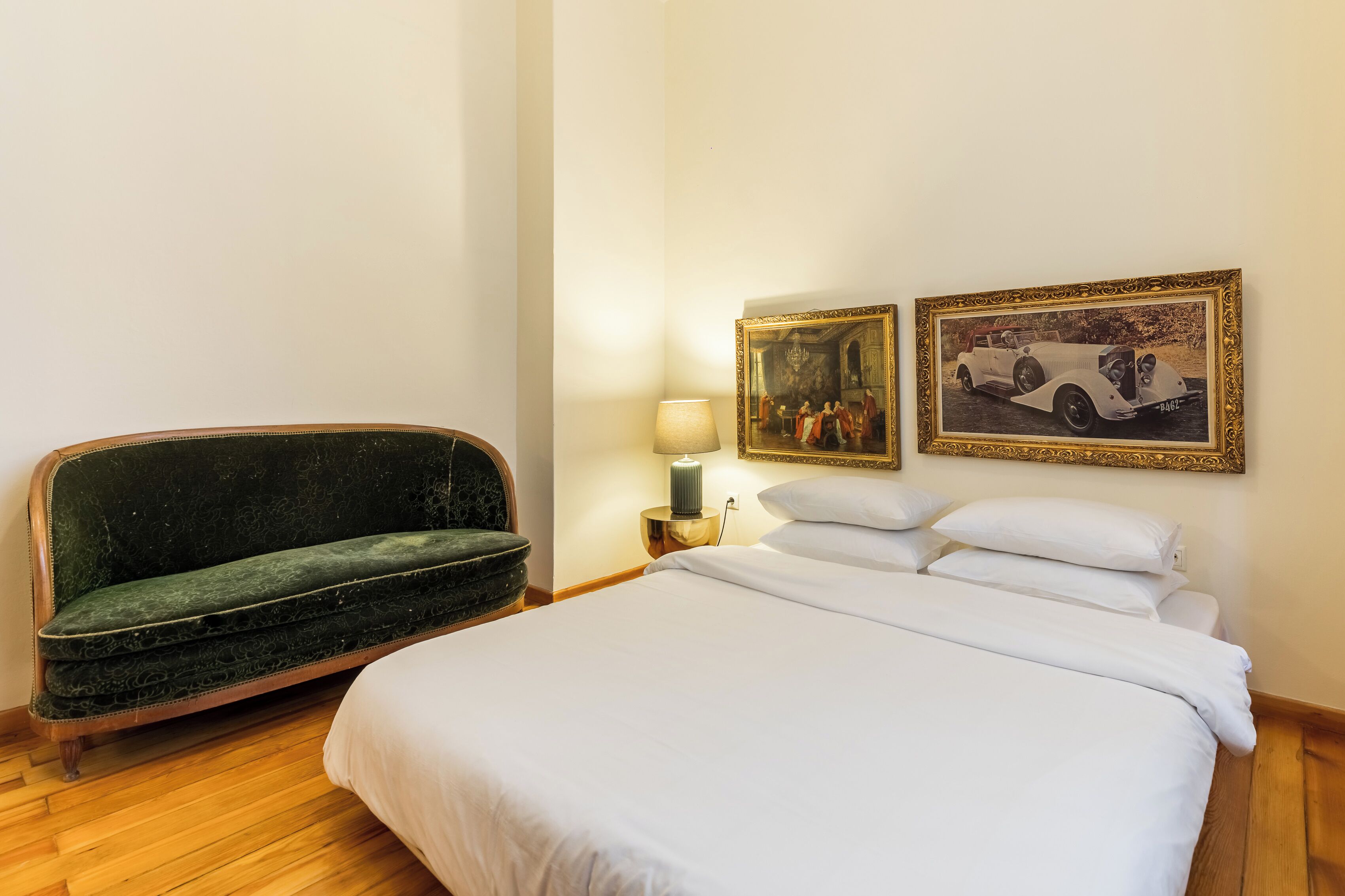 Une chambre d’hôtel avec un lit, un canapé vert, une table de chevet avec une lampe et deux tableaux encadrés au mur.