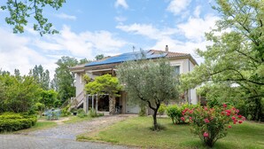 Ein Haus mit befestigter Auffahrt, einer überdachten Terrasse und einem Garten mit verschiedenen Pflanzen und Blumen.