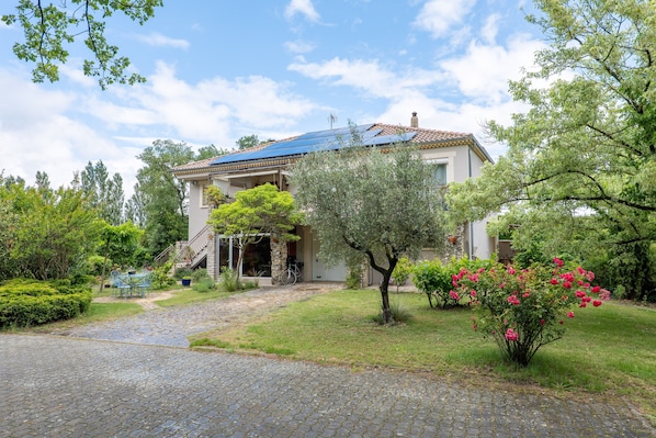 A house with a paved driveway, a covered patio, and a garden with various plants and flowers.