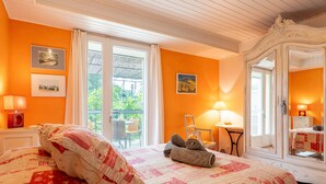 Ein Hotelzimmer mit Bett, Sessel, Tisch, Spiegel und einem Balkon mit Blick auf Grünflächen.