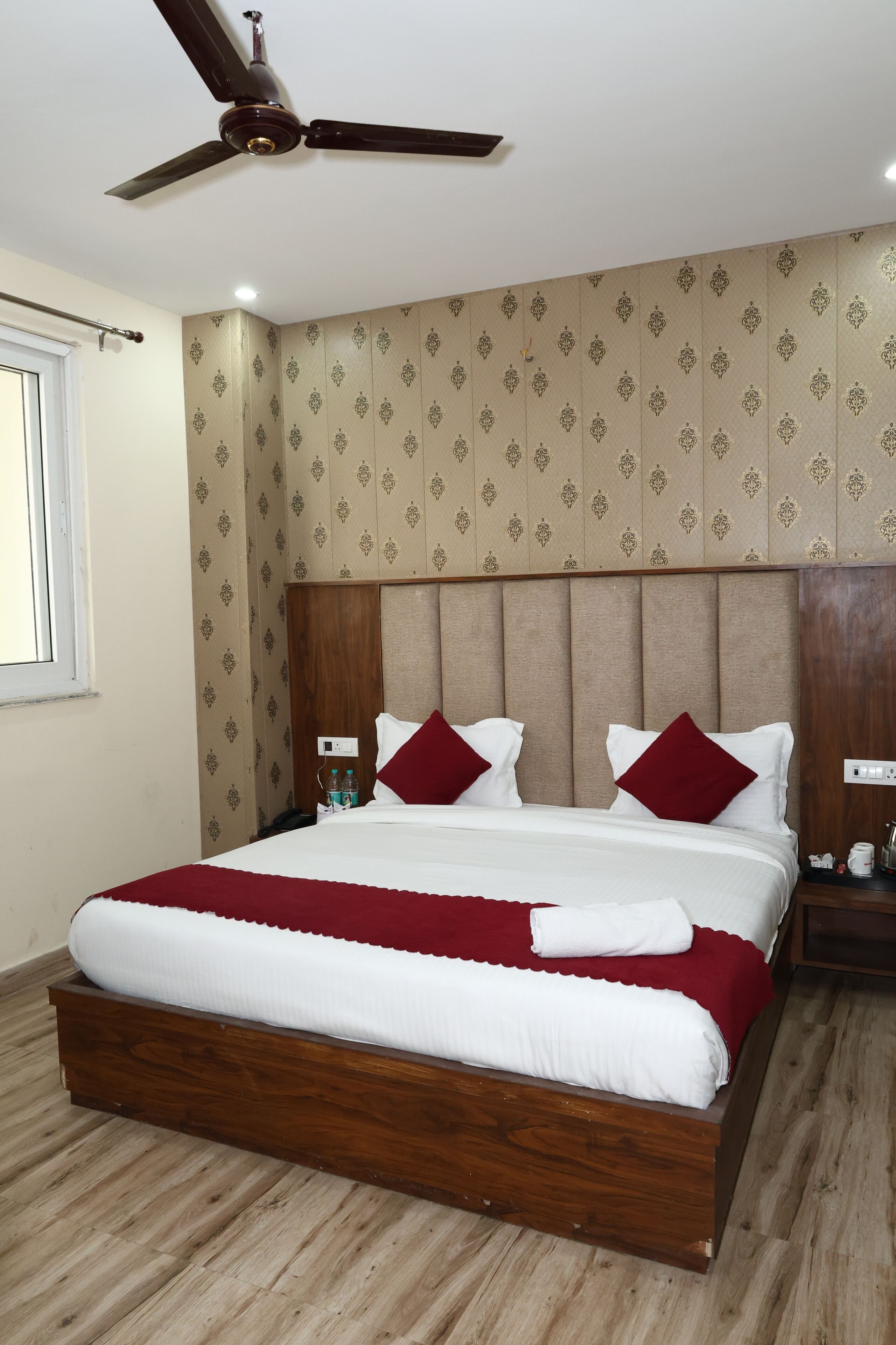 Una habitación de hotel con una cama grande, cabecera de madera, papel tapiz estampado y un ventilador de techo.