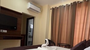 Una camera d'albergo con un letto grande, una ventola a soffitto, un condizionatore d'aria, una TV a schermo piatto montata a parete e una finestra con tende.