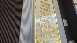 A wall with a plaque in a foreign language, a clock, and a vent. - Hotel Vardhman (Ujjain)
