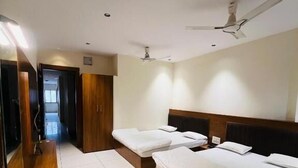 A hotel room with two single beds, a wooden bench, a large mirror, and a ceiling fan. - Hotel Vardhman (Ujjain)