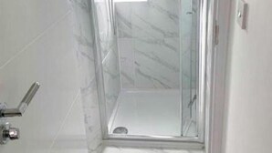 A glass-enclosed shower with a marble floor and walls, a visible window, and a door with a handle.