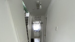A narrow hallway with white walls, a radiator, and a staircase leading to a landing.