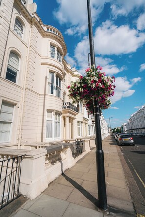 A row of classic white buildings with balconies, a clear blue sky, and a flower basket on a pole. - Big Apartment in Paddington - Central London - Families :) (London)