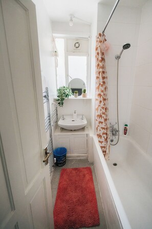 A narrow bathroom with a white sink, a shower with a patterned curtain, and a red rug. - Big Apartment in Paddington - Central London - Families :) (London)