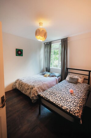 A bedroom with two beds, a window with curtains, a wall-mounted light fixture, and a framed picture. - Big Apartment in Paddington - Central London - Families :) (London)