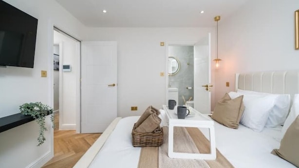 A modern bedroom with a bed, bedside table, and a TV mounted on the wall. - Premium - 1 BR Flat with Terrace (Kentish Town)