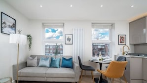 A modern apartment with a grey sofa, two chairs, a dining table, and a kitchen area. - Premium - 1 BR Flat with Terrace (Kentish Town)