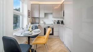 A modern kitchen with white cabinets, a dining table with chairs, and a window providing natural light. - Premium - 1 BR Flat with Terrace (Kentish Town)