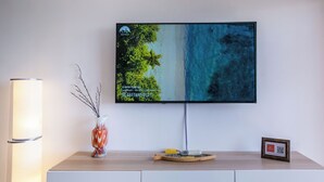 A flat-screen TV mounted on a wall above a wooden console with a vase and a framed picture. - RelaxInCyprus 1-bedroom apartment in awesome Pegeia with WiFi, AC (Pegeia)