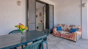 Une terrasse ouverte avec une table et des chaises, un canapé agrémenté de coussins à motifs et une porte donnant sur une autre pièce.