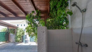 Un espace de douche extérieur abrité, avec des murs carrelés, un plafond en bois et une plante verte.