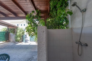 A covered outdoor shower area with tiled walls, a wooden ceiling, and a green plant.