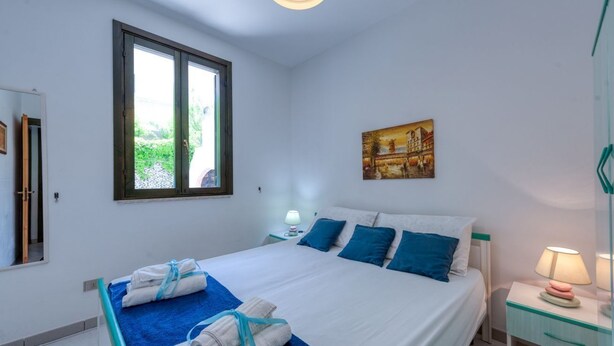 Une chambre d’hôtel avec un lit, une table de chevet avec une lampe, une fenêtre donnant sur un paysage et un tableau au mur.
