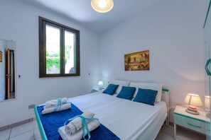 Ein Hotelzimmer mit Bett, Nachttisch mit Lampe, Fenster mit Blick und einem Bild an der Wand.