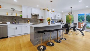 Una cocina moderna con armarios blancos, una isla central con taburetes y una zona de comedor con vista a un lago.