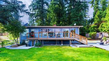 A modern two-story house with a deck, surrounded by lush greenery and tall trees.