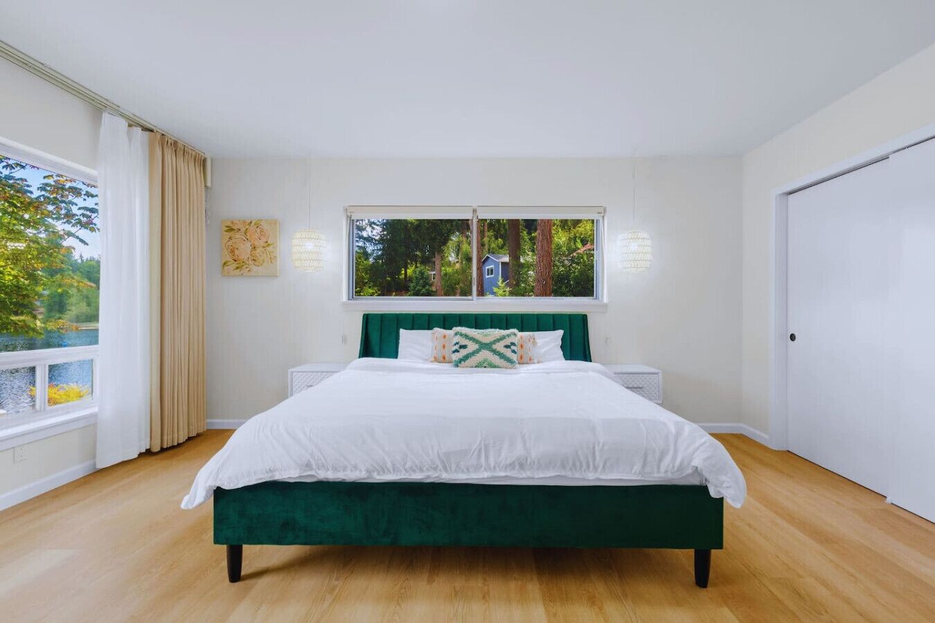 Un dormitorio con una cama tapizada de verde, ropa de cama blanca, una ventana con vistas a árboles y una puerta blanca.