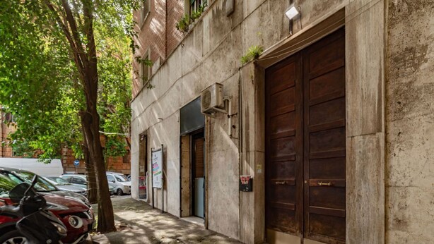 A building with large wooden garage doors, a tree, and parked motorcycles. - GuestHost - Cozy apartment of about 70 sqm, able to accommodate up to 4 people, located on the fourth floor of a building with a lift (NOT suitable for disabled people).The property is located in the Flaminio district, close to the Lungotevere, in a well (Rome)