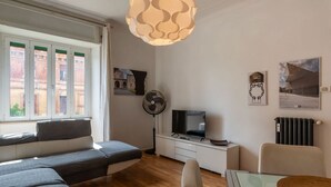 A modern living room with a sofa, a dining table, a TV, and artwork on the walls. - GuestHost - Cozy apartment of about 70 sqm, able to accommodate up to 4 people, located on the fourth floor of a building with a lift (NOT suitable for disabled people).The property is located in the Flaminio district, close to the Lungotevere, in a well (Rome)
