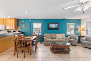 Un salon moderne avec un mur de couleur turquoise, une table basse ronde, un canapé et un coin repas avec des chaises et une table en bois.