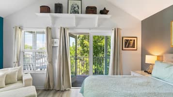 Quarto com cama, mesa de cabeceira, luminária, janela com cortinas e varanda com guarda-corpo.
