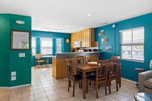 Une cuisine aux murs de couleur turquoise, avec des meubles en bois, un îlot central et un coin repas équipé de chaises.