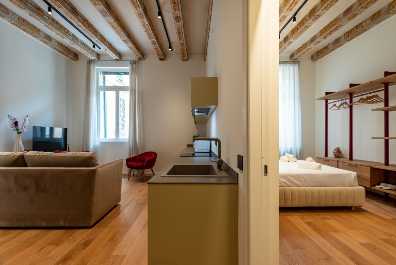 A modern hotel room with a sofa, a small kitchen area, a bed, and a TV.