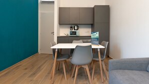 A compact kitchen with a white countertop, grey cabinets, and a microwave. There are four grey chairs around the table, and a grey sofa in the foreground. - Superior Studio | Hotiday Torino OGR (Turin)