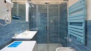 A modern bathroom with a glass-enclosed shower, a white sink, and a blue towel rack. - Superior Studio | Hotiday Torino OGR (Turin)