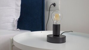 A bedside table with a clear glass bulb lamp on a white surface. - Superior Studio | Hotiday Torino OGR (Turin)
