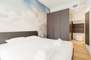 A hotel room with a large bed, a wardrobe, a small bathroom, and a wall with a cloud-like mural.