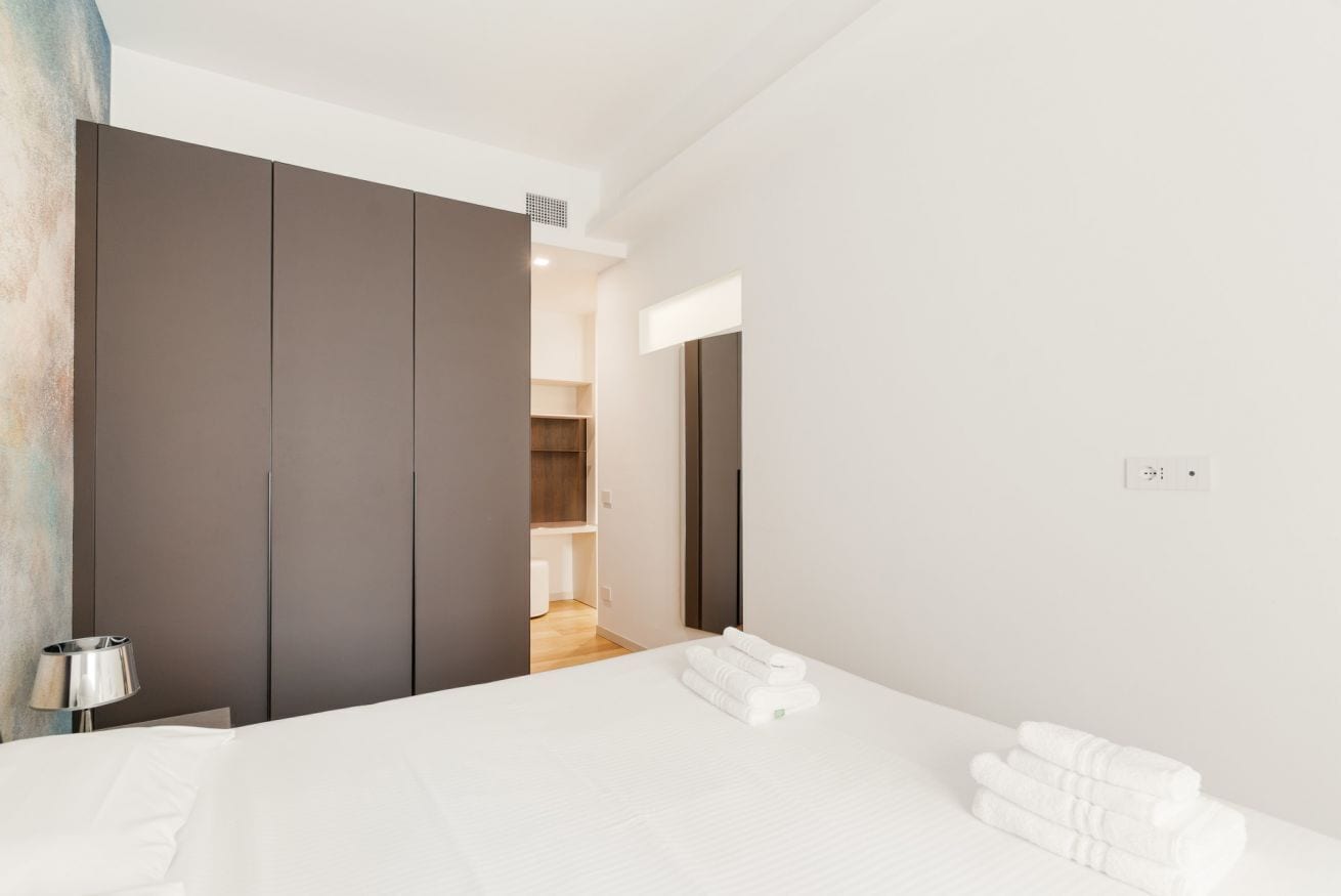 A modern hotel room with a large bed, a wardrobe, and a bathroom visible through an open door.