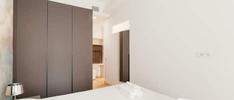A modern hotel room with a large bed, a wardrobe, and a bathroom visible through an open door.