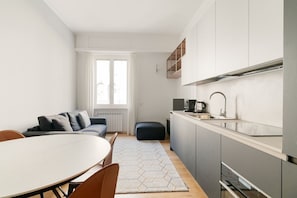 A modern kitchen with a dining area, a sofa, and a window.