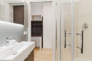 A modern bathroom with a white sink, mirror, and glass shower enclosure.