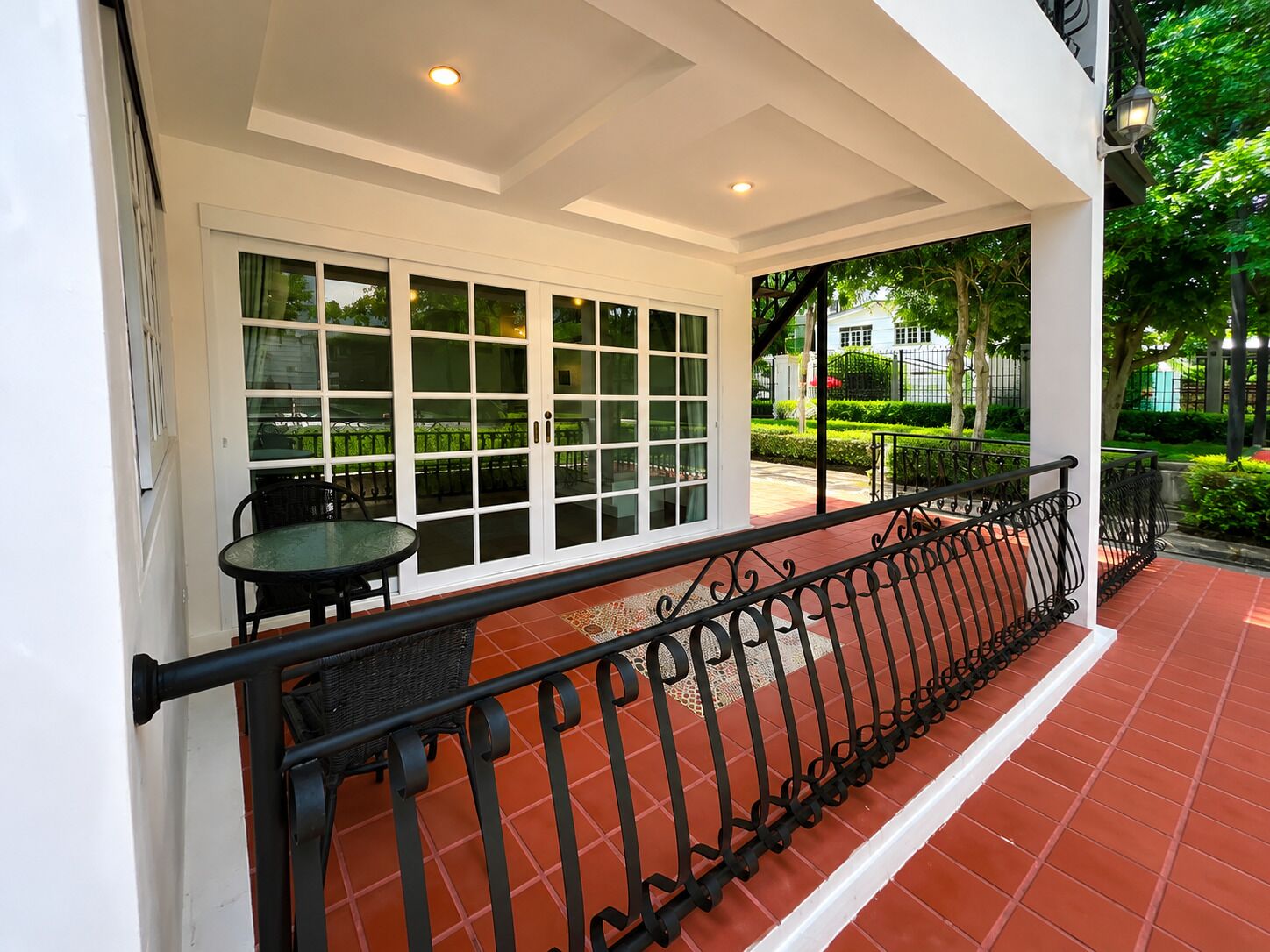 A covered outdoor seating area with a table and chairs, a railing, and a view of the garden.