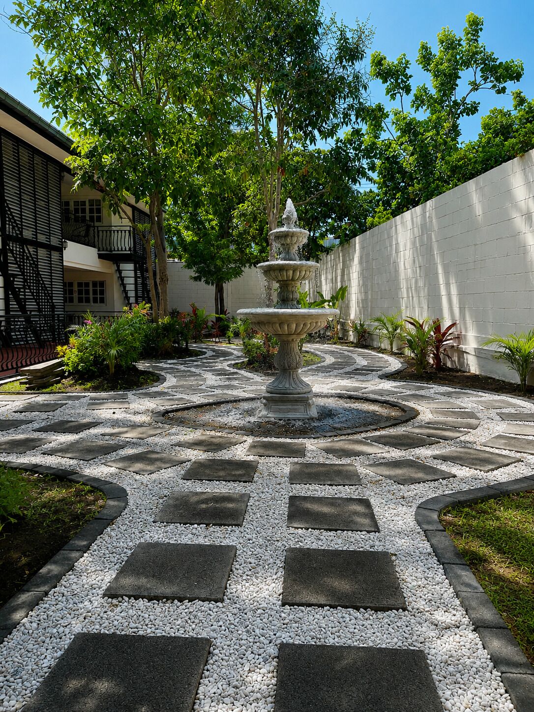 A courtyard with a central fountain, surrounded by a stone pathway and bordered by a white wall.