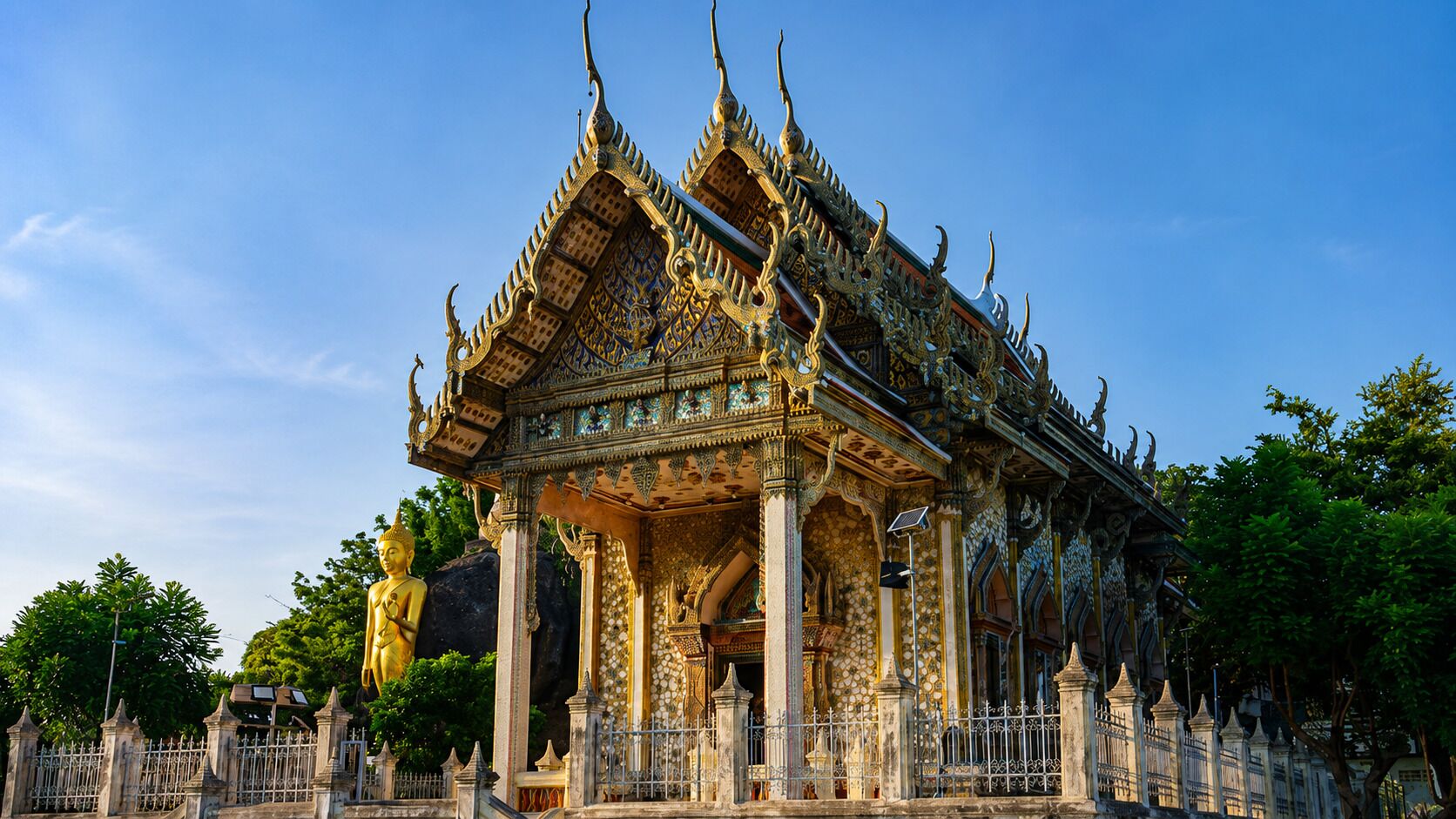 A traditional Thai temple with ornate architecture, a large Buddha statue, and a surrounding fence.